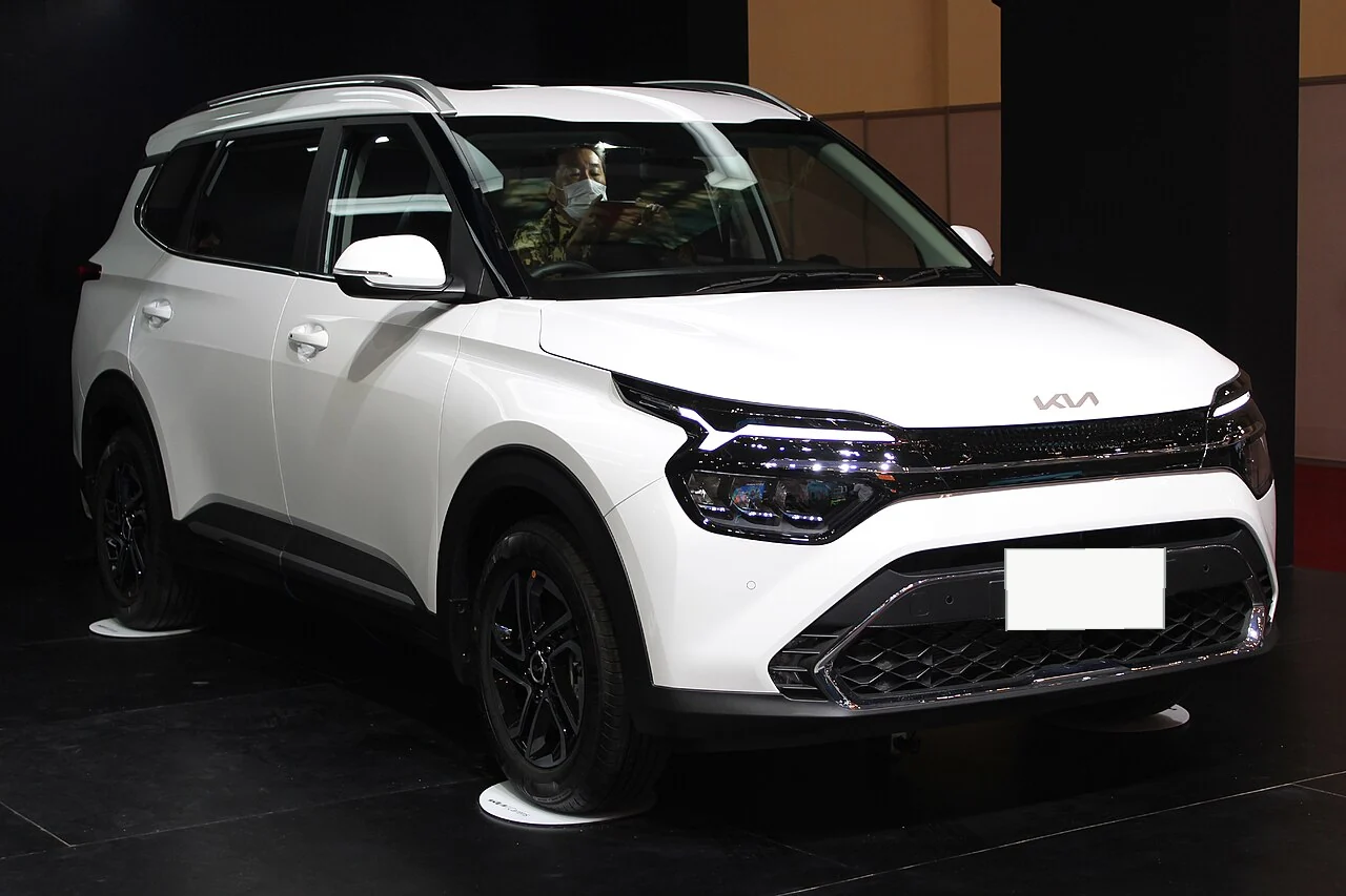 Representative photo of a white Kia Carens family MPV displayed at an auto show; actual vehicle availability is confirmed directly